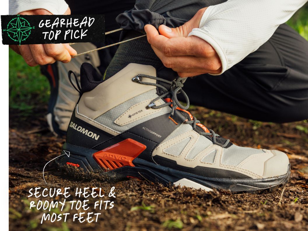 A man wearing new boots squats on a trail. Text overlay reads: Gearhead Top Pick, secure heel & roomy toe fits most feet.
